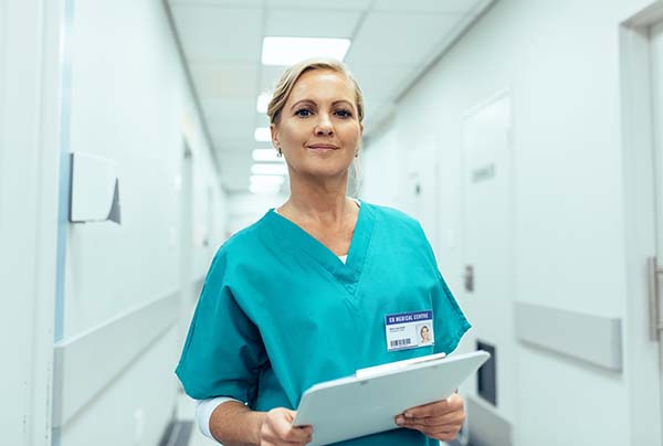 Woman healthcare worker with clipboard in corridor.